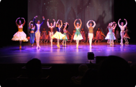 Bailarinos no palco durante apresentação, todos estão com fantasias lembrando de príncipes e princesas da Disney.